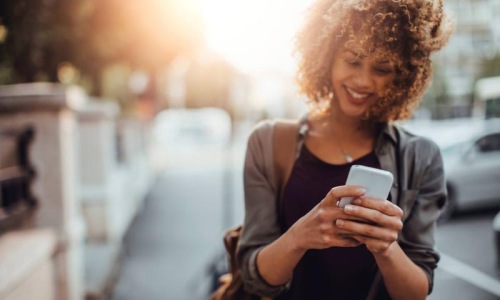 woman texts on her phone as she walks through the city